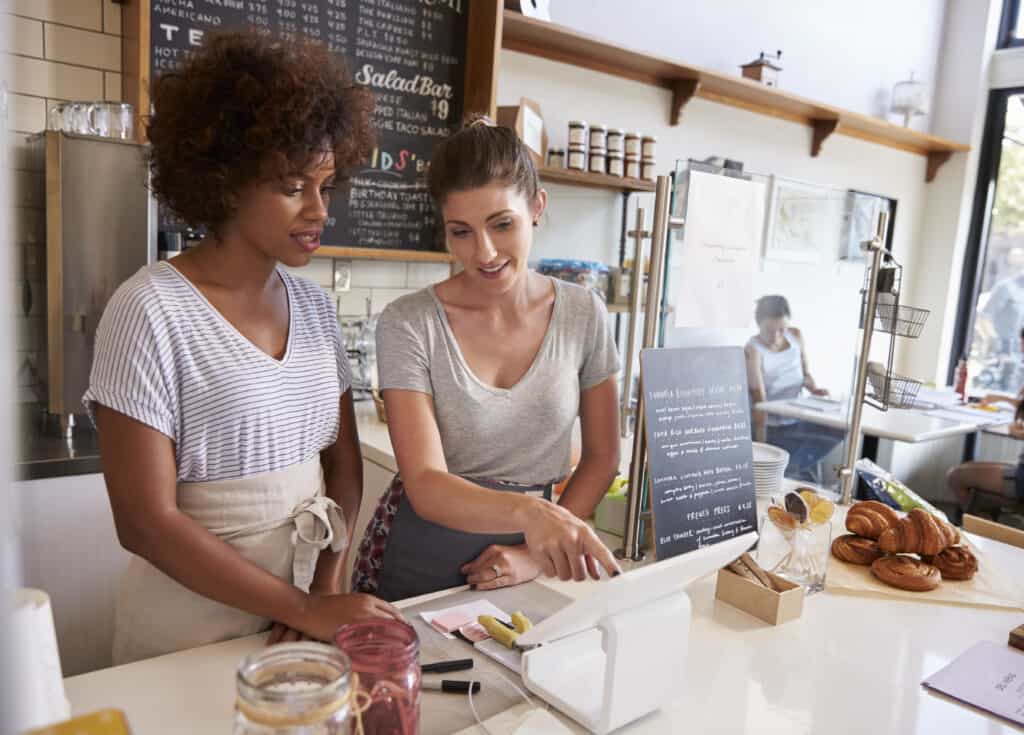 Waitress showing new employee the till at a coffee shop