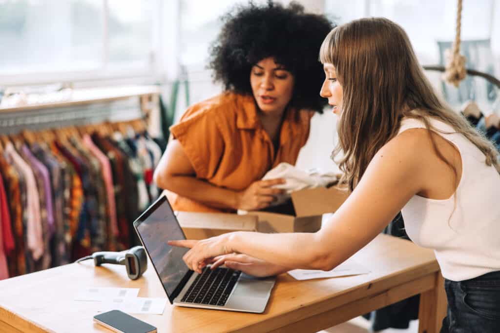 Online store owners having a discussion while using a laptop in their thrift store.